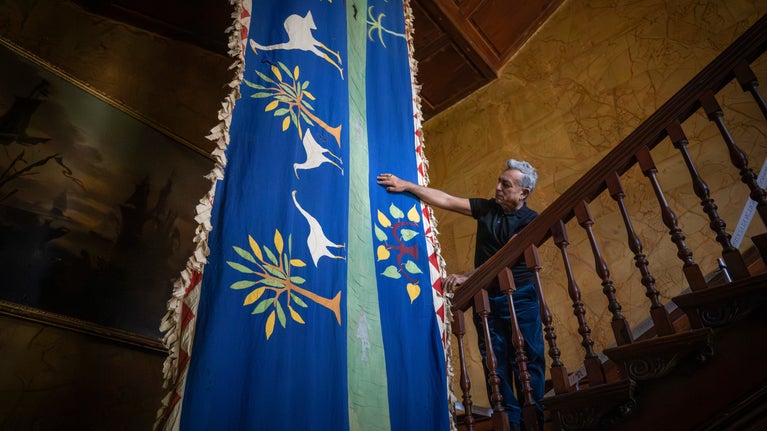 Karun Thakar stands on a grand staircase, admiring a blue flag which hangs past him from the ceiling
